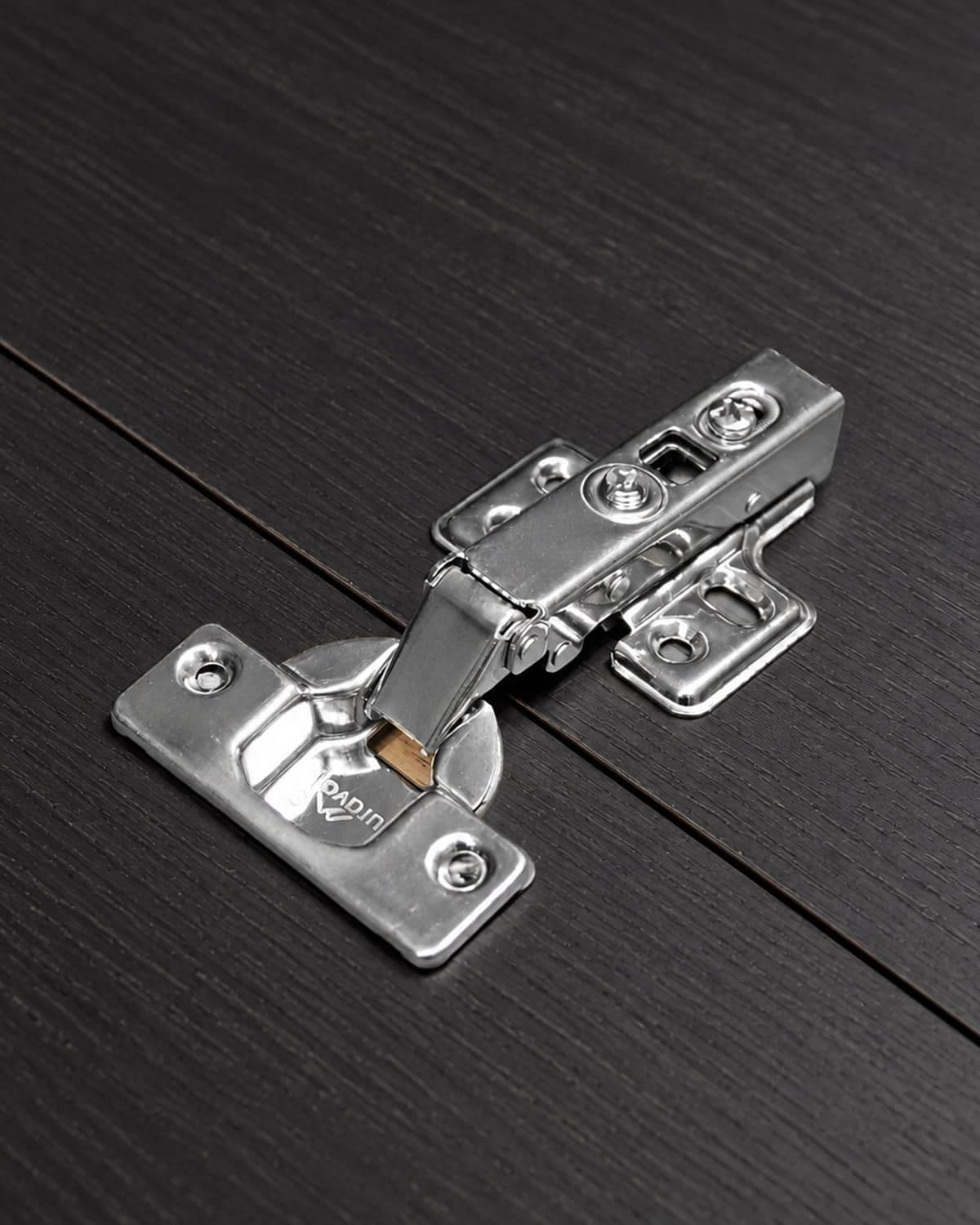 Bản lề giảm chấn Duraval đặt trên mặt gỗ sẫm màu