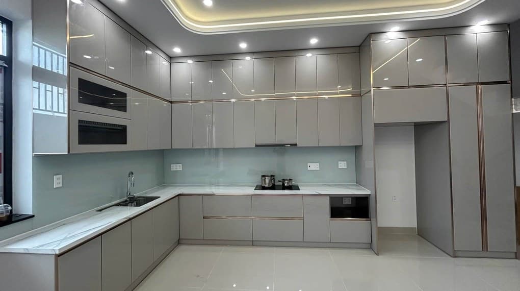Tủ bếp chữ L cánh acrylic xám bóng, tủ trên kịch trần, kính ốp bếp xanh nhạt