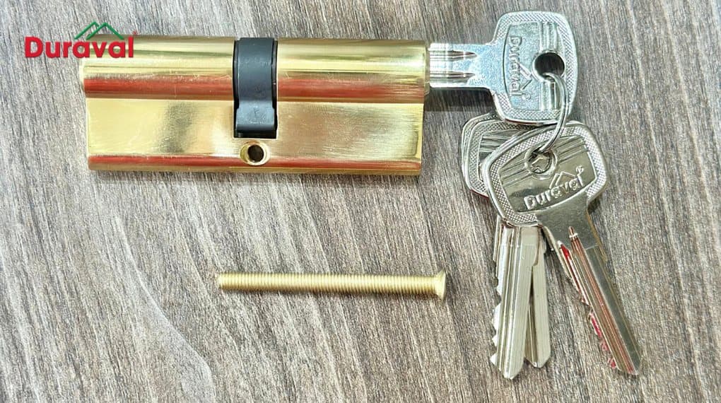 Ổ khóa cửa đồng hai đầu chìa Duraval H114 đặt trên mặt gỗ, kèm chùm chìa và ốc bắt ổ khóa