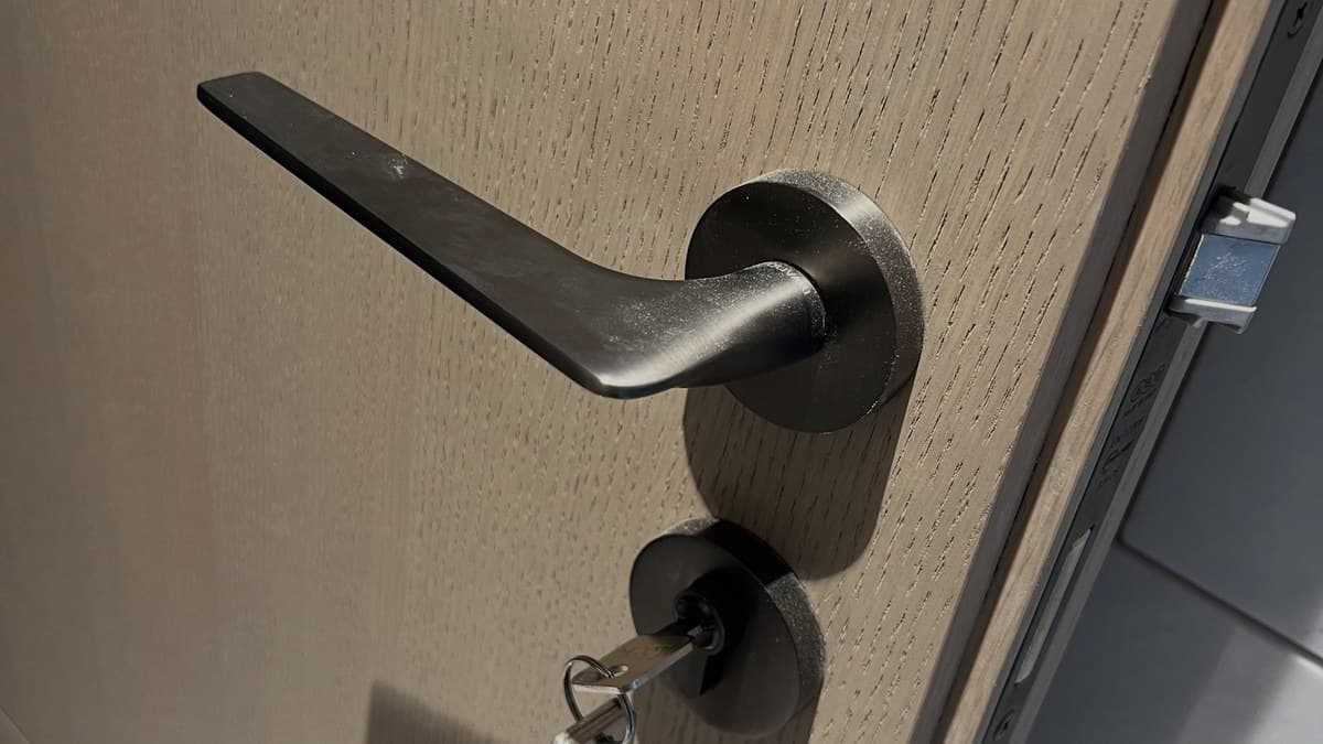 Cửa gỗ sồi lắp khóa tay gạt đen, bên dưới là ổ khóa đang cắm chìa
