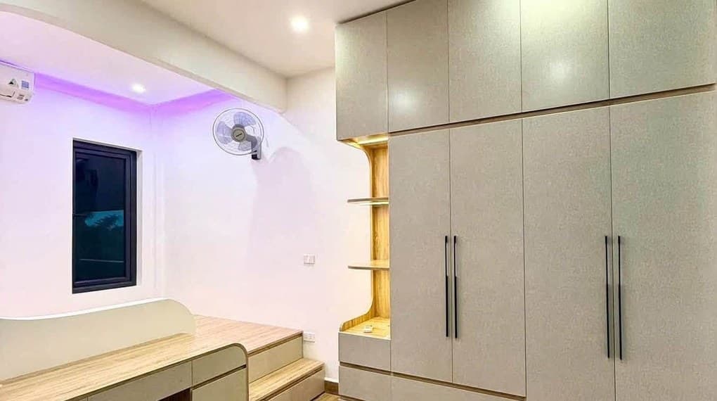 Phòng ngủ nhỏ có tủ áo kịch trần cánh phẳng màu xám, tay nắm dài, bàn học liền bục giường