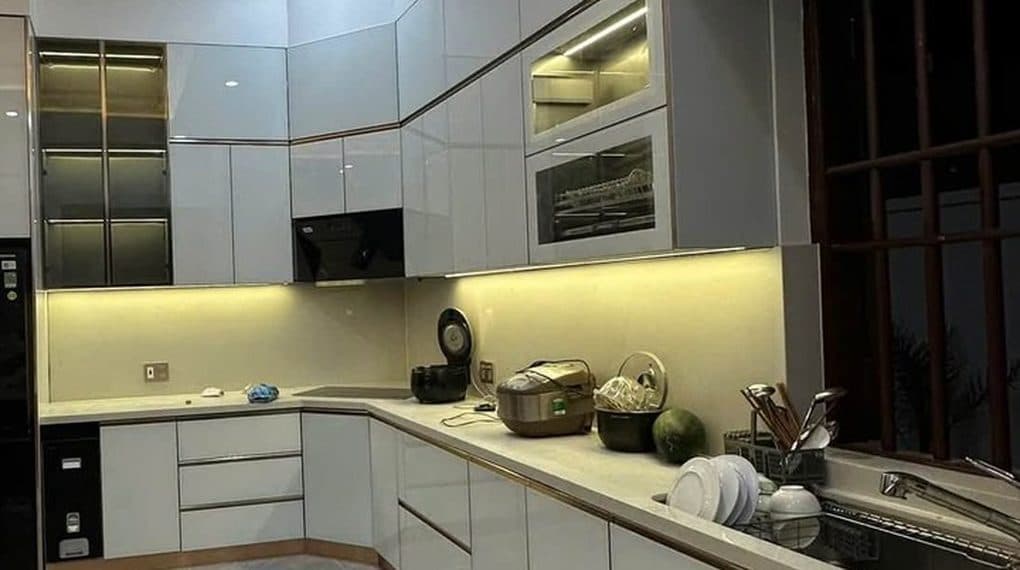 Tủ bếp chữ U màu xám trắng vừa lắp xong, đèn hắt dưới tủ trên đang bật, ảnh minh họa soi tủ bếp khi nhận nhà