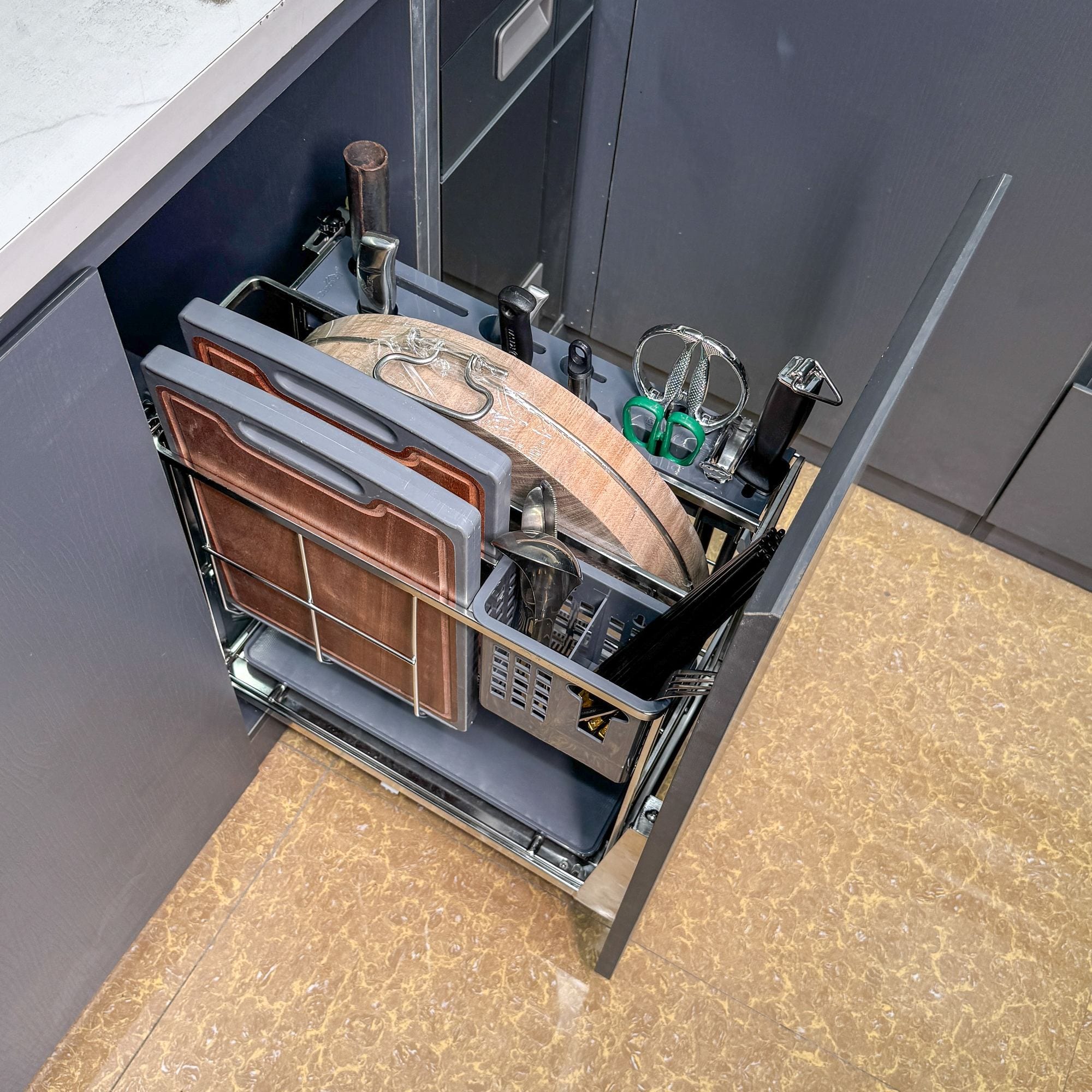 Ảnh chụp tại showroom Duraval: giá dao thớt inox 304 D6249 lắp trong tủ, kéo ra hết — thớt thái, thớt chặt, khay dao, giỏ đựng đa năng và khay hứng nước