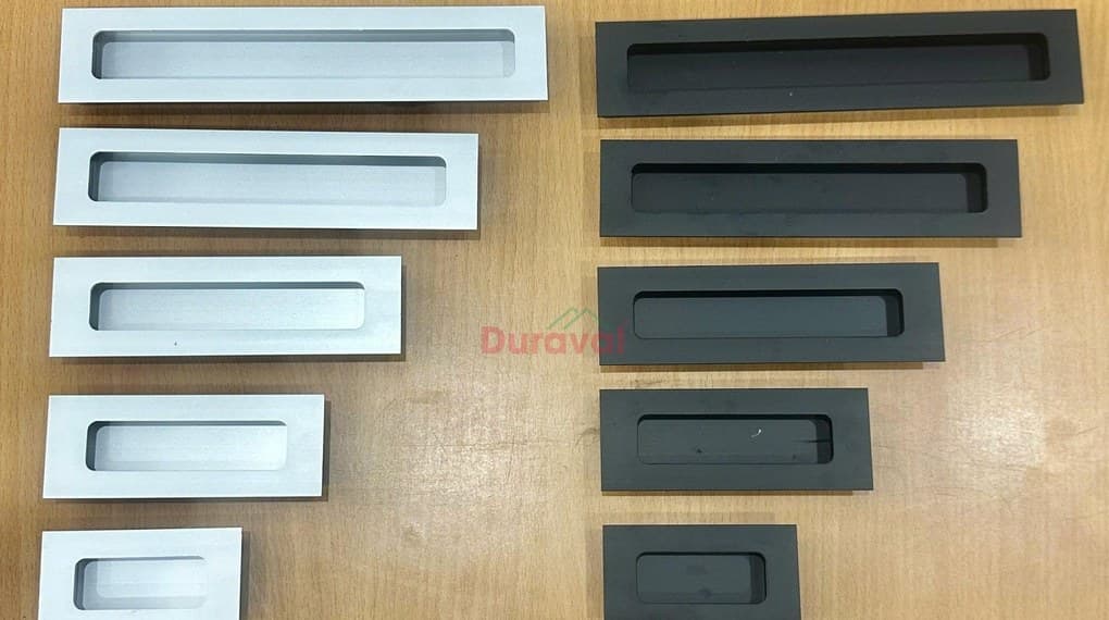 Tay nắm tủ âm Duraval D21 năm cỡ, màu trắng bạc và màu đen, xếp trên bàn gỗ