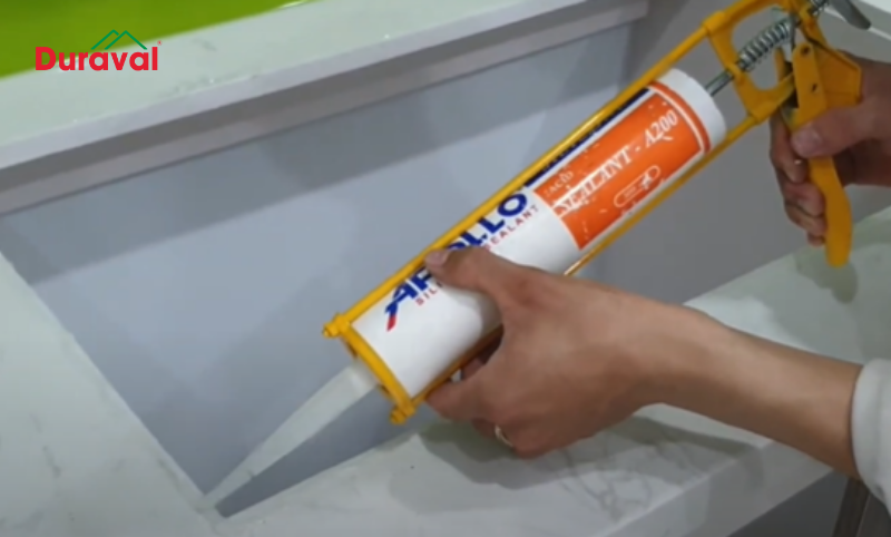 Bơm keo silicon quanh mép chậu hoặc quanh mép lỗ khoét sau đó hạ chậu xuống